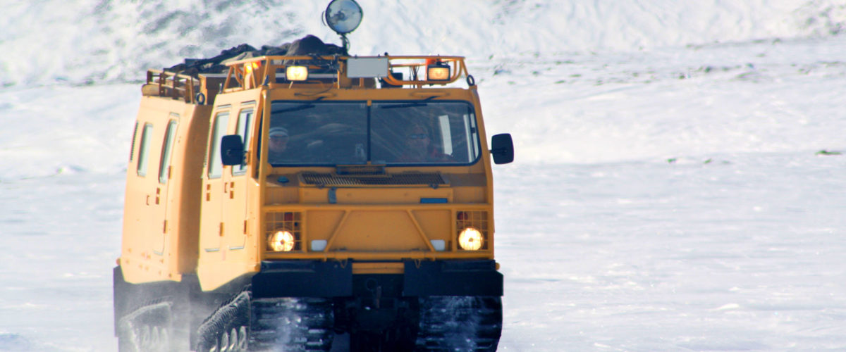 CBO employees driving a yellow BV206 all-terrain vehicle with track wheels on snow in the Arctic.