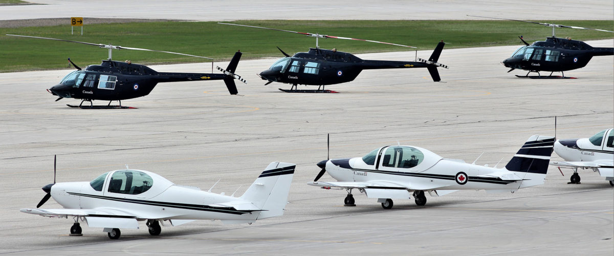 Helicopters and airplanes parked on a runway tarmac at CFTS Southport in Manitoba.