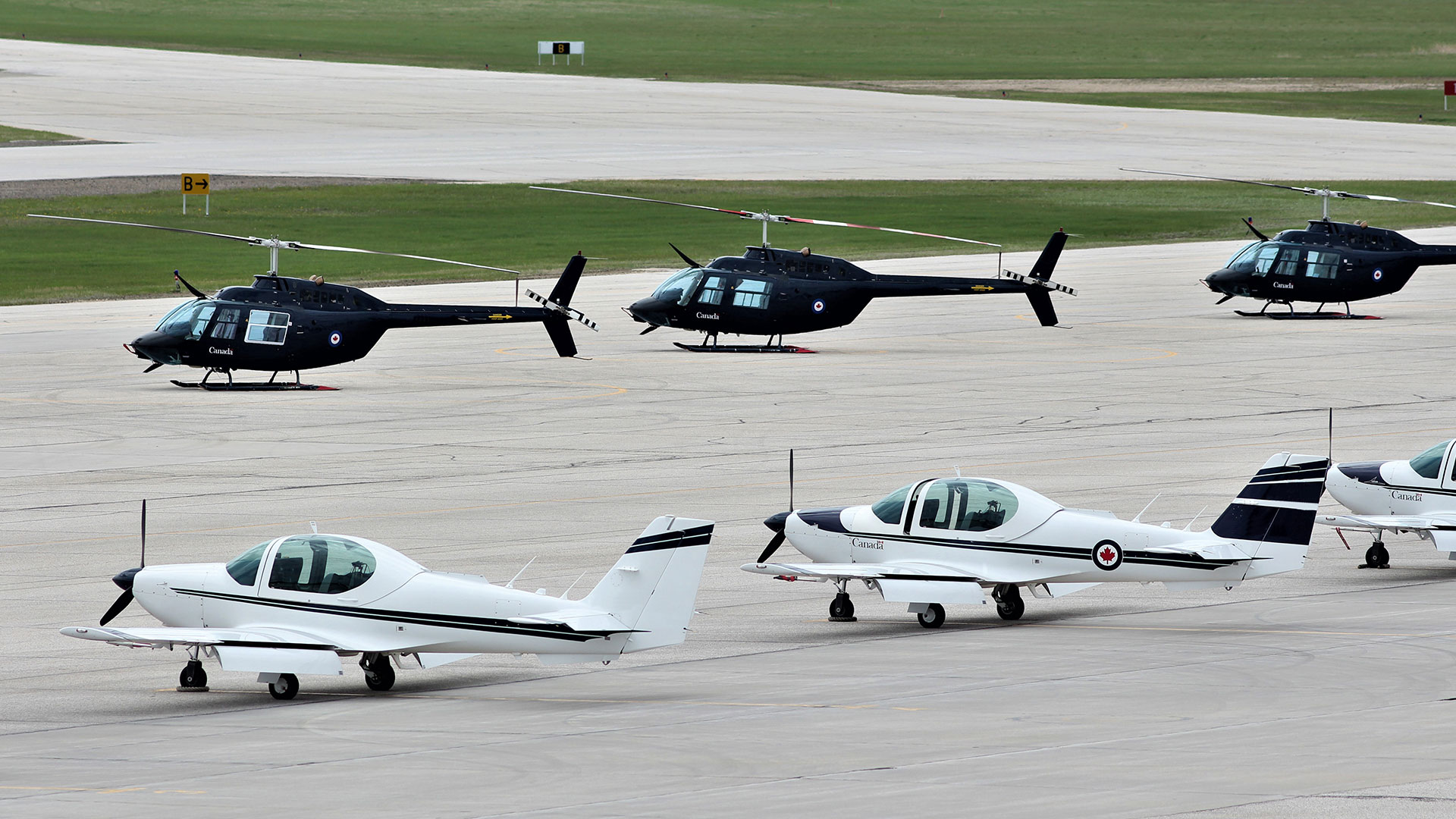 Three helicopters and two airplanes parked on a runway tarmac at CFTS Southport in Manitoba.