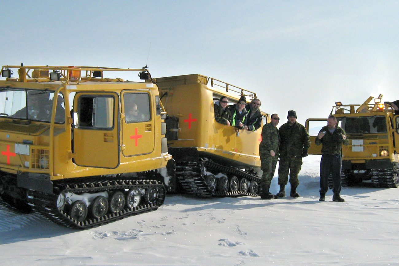 Image-Community CBO employees with two yellow BV206 all-terrain vehicles with track wheels on snow in the Arctic.