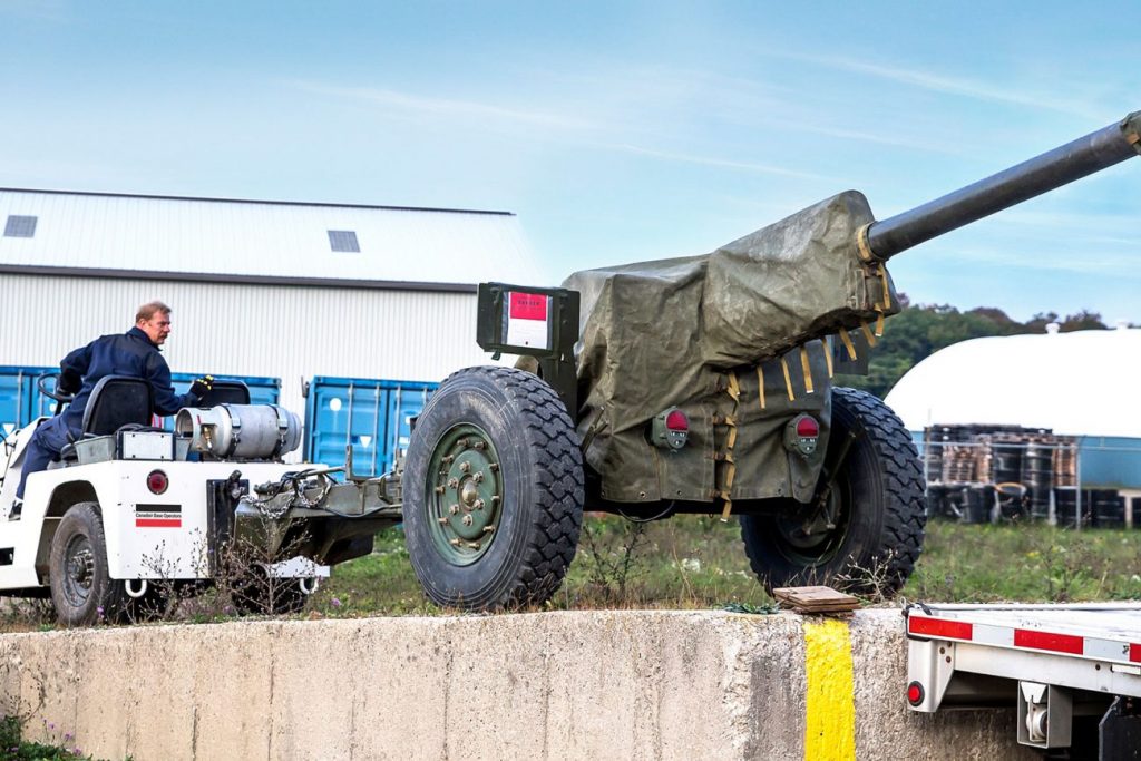 A CBO employee in a vehicle loading a Howitzer military gun onto a flatbed trailer.
