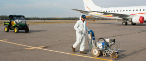 A CBO employee operating a line painting machine on an airfield runway.